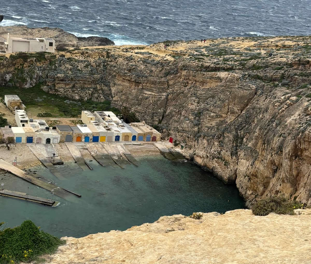 Aerial view of the Inland Sea at Dwejra, Gozo, showing the sheltered lagoon, boat houses and surrounding cliffs